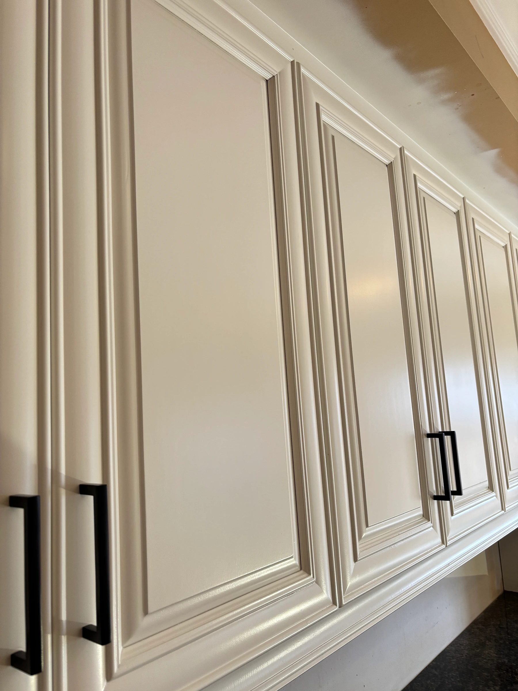 Close-up of smooth white cabinet doors with decorative trim and black handles